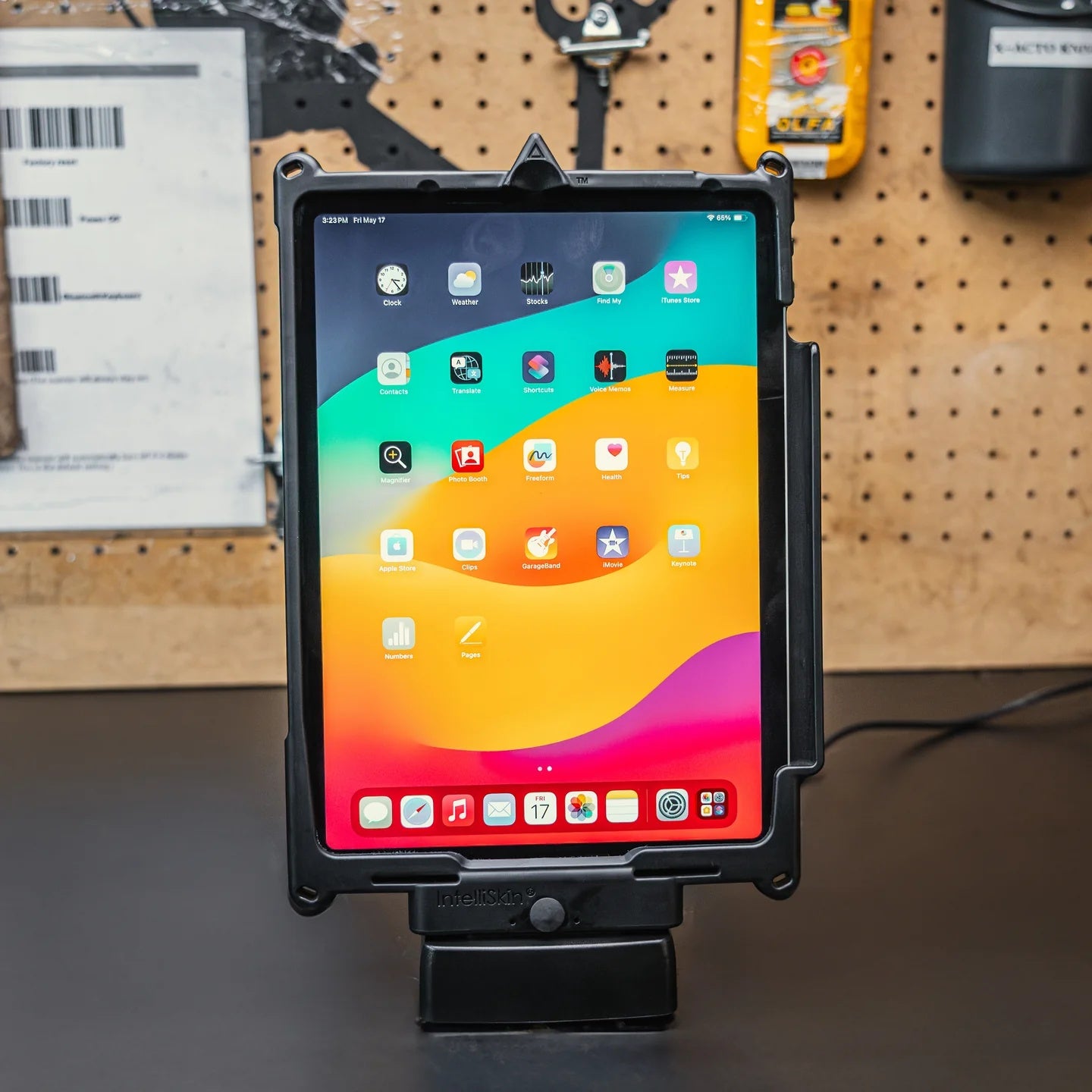 Tablet in a protective case on a GDS charging dock with a colorful display of app icons against a wooden pegboard background.